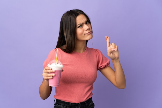 Teenager girl holding a strawberry milkshake with fingers crossing and wishing the best