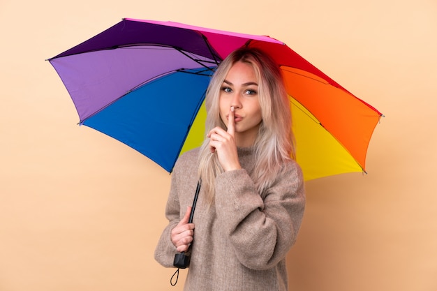 Teenager girl holding an umbrella over wall doing silence gesture