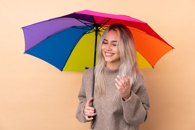 Teenager girl holding an umbrella over wall laughing