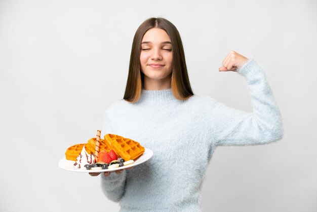 Teenager girl holding waffles over isolated white background doing strong gesture