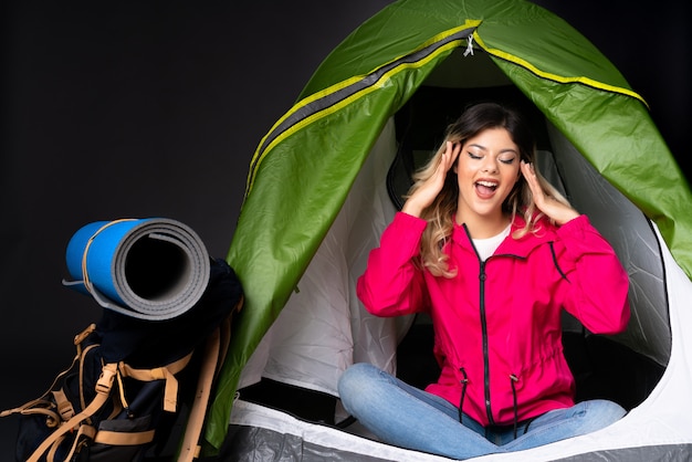 Teenager girl inside a camping green tent on black wall with surprise dexpression