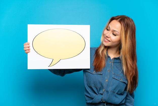 Teenager girl over isolated blue background holding a placard with speech bubble icon