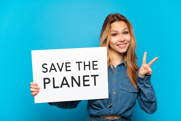 Teenager girl over isolated blue background holding a placard with text Save the Planet and celebrating a victory