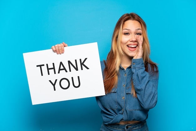 Teenager girl over isolated blue background holding a placard with text THANK YOU and shouting