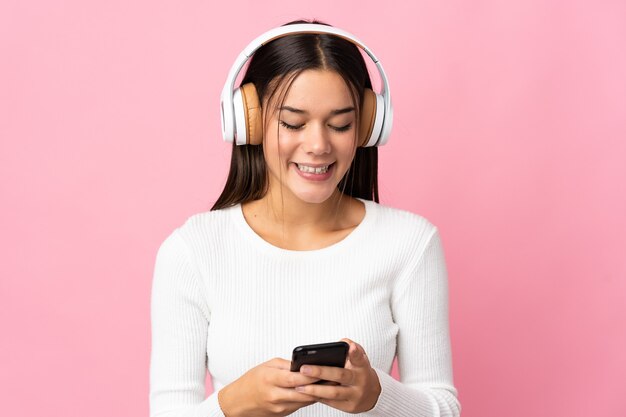 Teenager girl isolated on blue listening music and looking to mobile