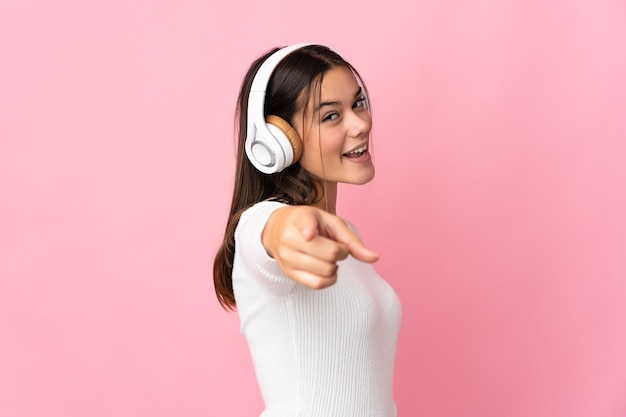 Teenager girl isolated on blue listening music and pointing to the front