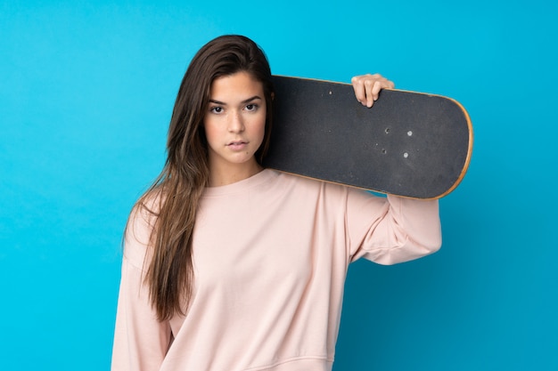 Teenager girl over isolated blue wall with a skate