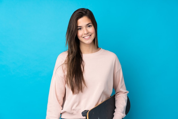 Teenager girl over isolated blue wall with a skate