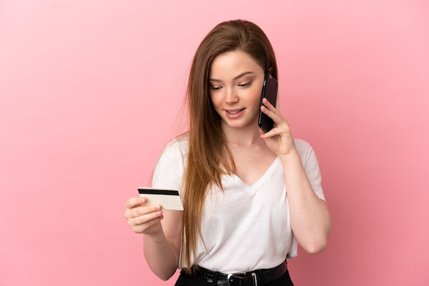 Девушка-подросток на изолированном розовом фоне покупает с мобильного телефона с помощью кредитной карты