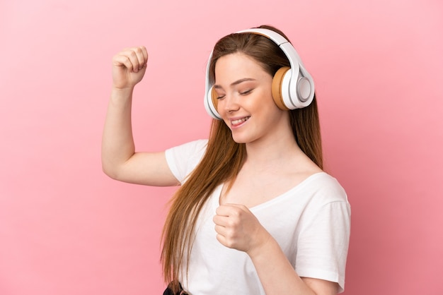 Teenager girl over isolated pink background listening music and dancing