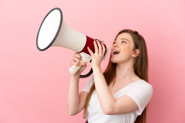 Teenager girl over isolated pink background shouting through a megaphone to announce something in lateral position