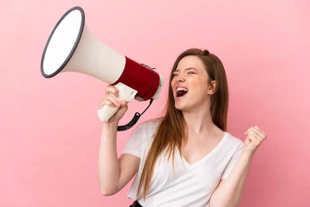 Teenager girl over isolated pink background shouting through a megaphone to announce something in lateral position