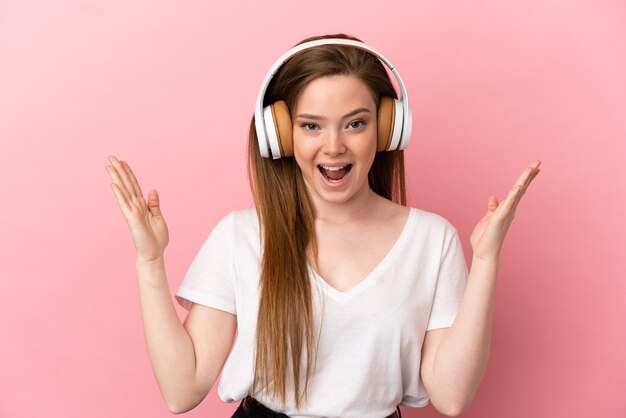 Teenager girl over isolated pink background surprised and listening music