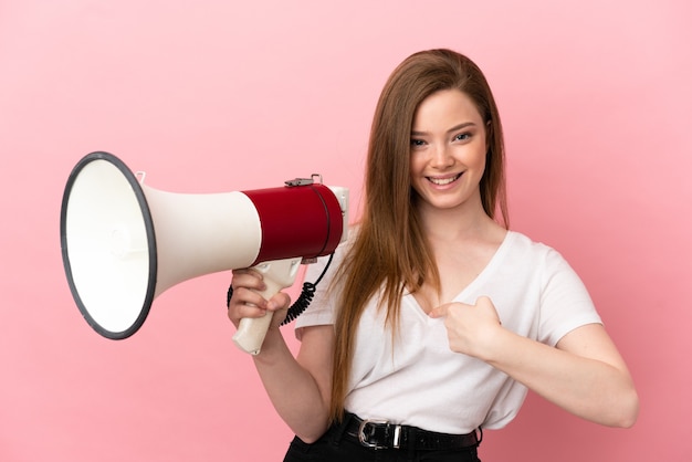 Ragazza dell'adolescente sopra la superficie rosa isolata che tiene un megafono e con l'espressione facciale di sorpresa