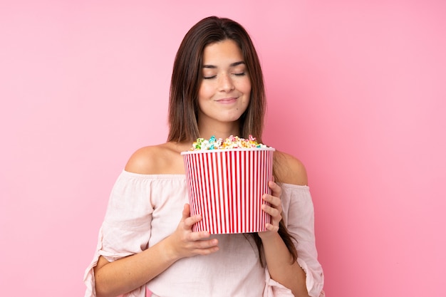 Teenager girl over isolated pink wall holding a big bucket of popcorns