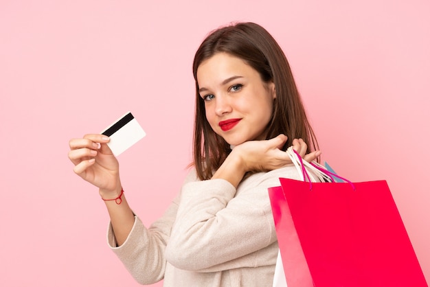 쇼핑백과 신용 카드를 들고 분홍색 벽에 고립 된 십 대 소녀