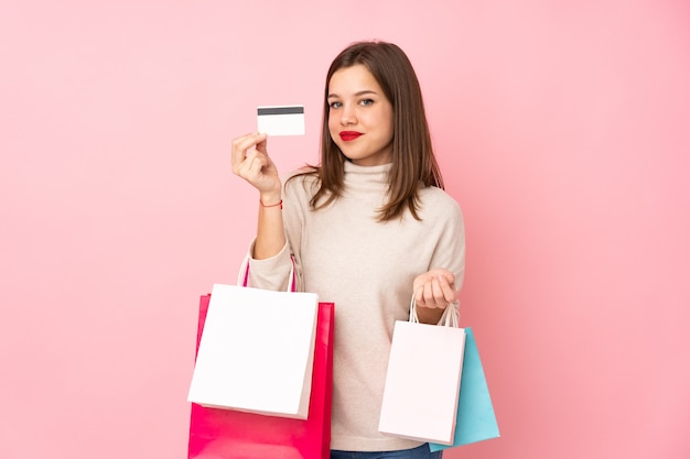 Foto ragazza dell'adolescente isolata sui sacchetti della spesa rosa della tenuta della parete e una carta di credito