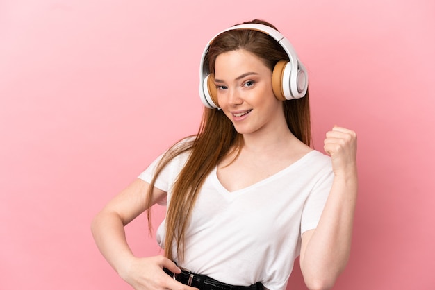 Teenager girl over isolated pink wall listening music and doing guitar gesture