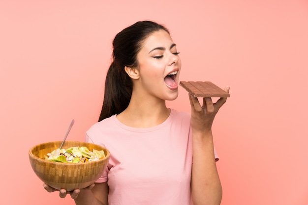 Teenager girl  over isolated pink wall with salad and chocolat