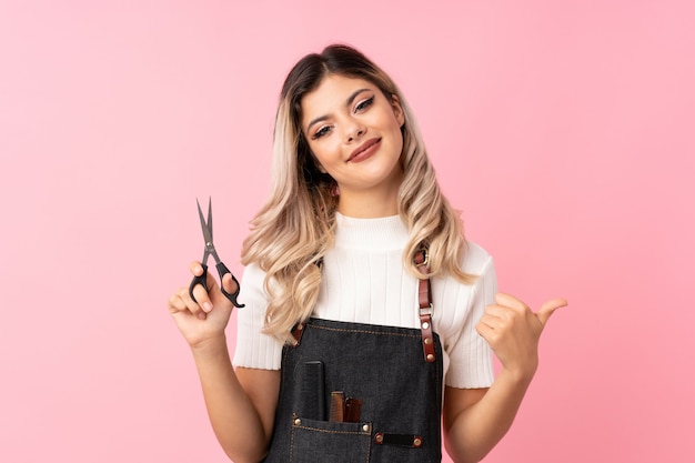 Foto ragazza dell'adolescente sopra il rosa isolato con il parrucchiere o il vestito da barbiere e indicarlo