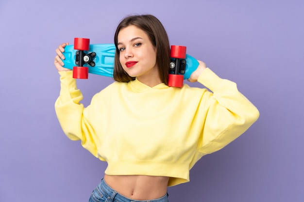 Teenager girl isolated on purple wall with a skate