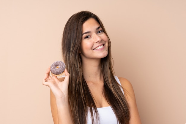 Teenager girl over isolated wall holding a donut and happy