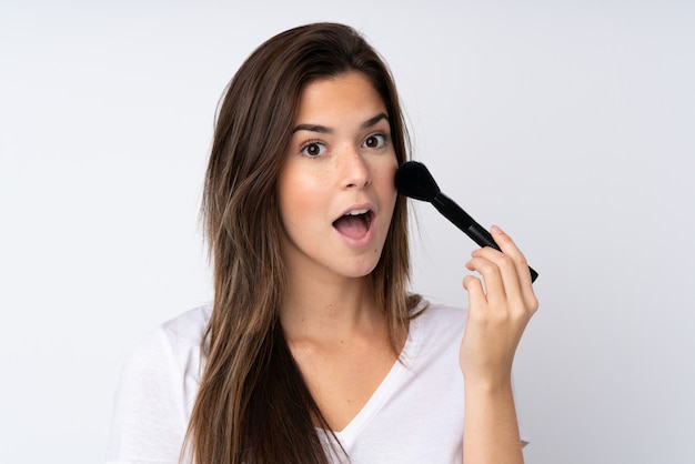 Teenager girl over isolated wall holding makeup brush and surprised