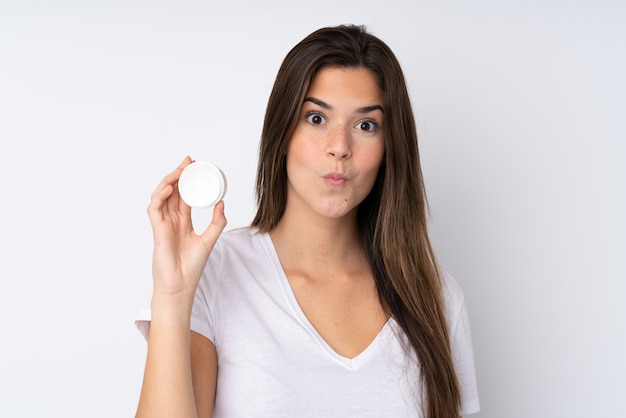 Teenager girl over isolated wall with moisturizer