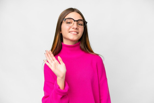 Teenager girl over isolated white background saluting with hand with happy expression