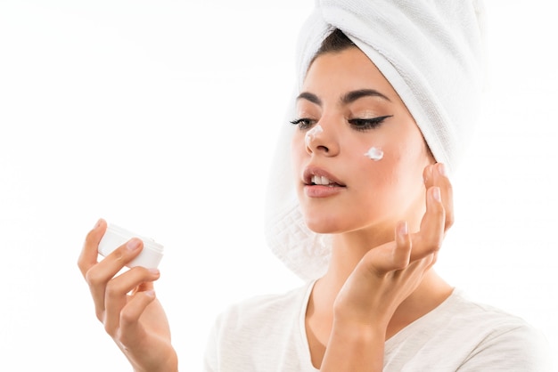 Teenager girl over isolated white wall with moisturizer