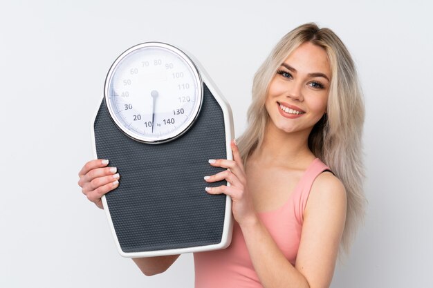 Teenager girl over isolated white wall with weighing machine