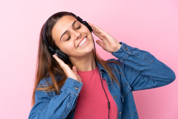 Teenager girl listening music and dancing over isolated pink wall