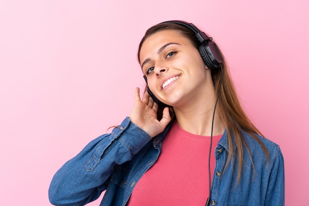 Teenager girl listening music over isolated pink wall