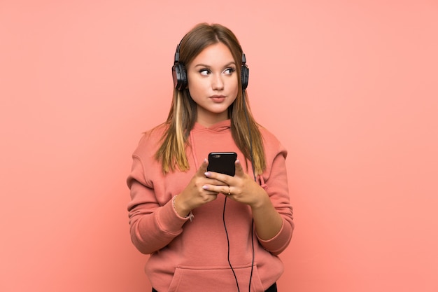 Teenager girl listening music with a mobile over isolated pink wall