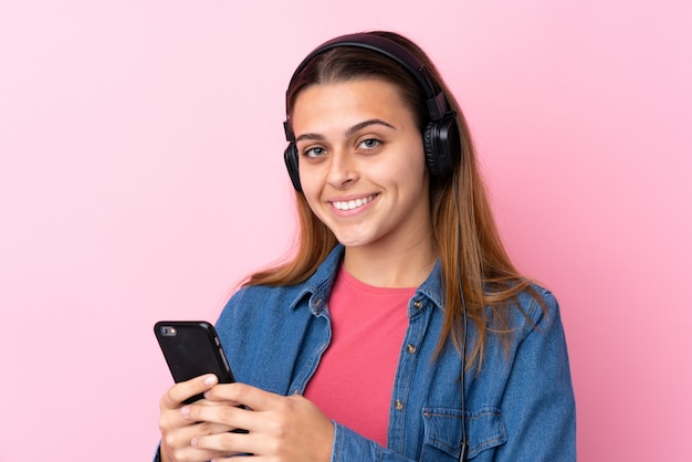 Musica d'ascolto della ragazza dell'adolescente con un cellulare sopra la parete rosa isolata