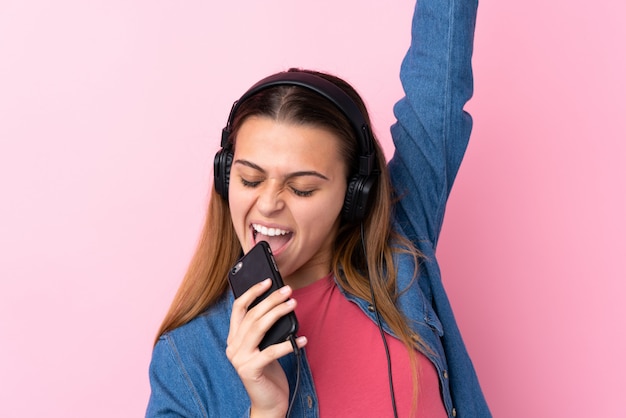 Девушка подростка слушая музыка с чернью над изолированной розовой стеной