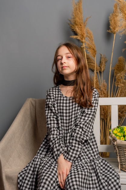 Teenager girl looking at the camera indoors. Portrait of beautiful teenage girl in dress over gray.