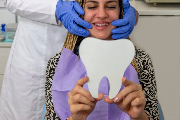 Teenager girl looking at her braces and teeth in the mirror at dentists of happy patients and dentists