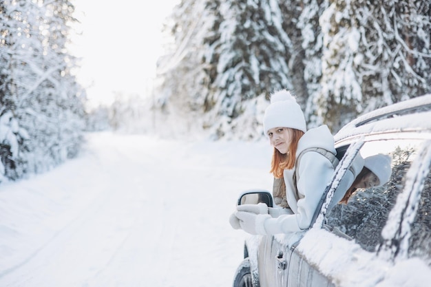 Teenager girl looking out of car window traveling in winter snowy forest Road trip adventure and local travel concept Happy child enjoying car ride Christmas winter holidays and New year vacation