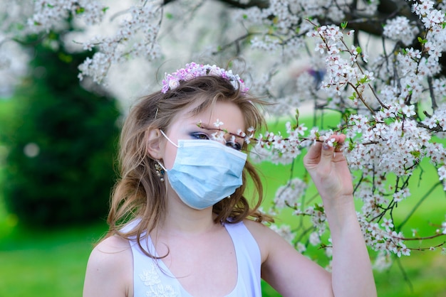 春の花の咲く庭園で医療マスクのティーンエイジャーの女の子