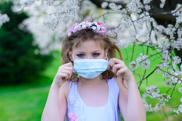 Teenager girl in medical mask in spring flowering garden.