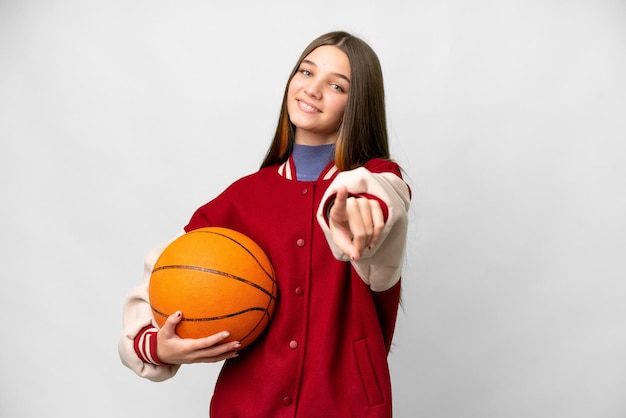 Teenager girl playing basketball over isolated white background pointing front with happy expression