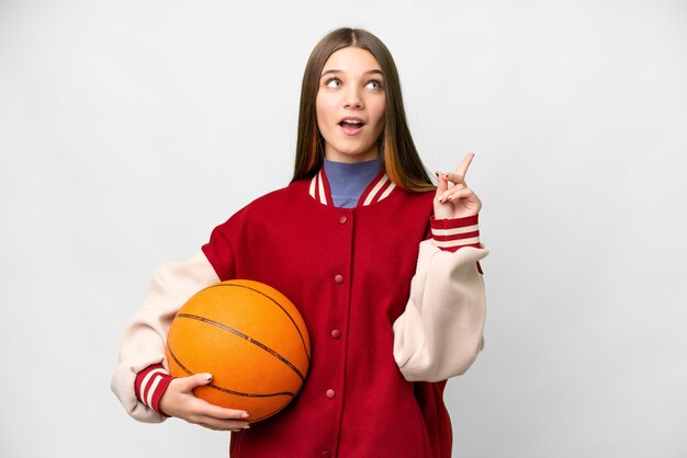 Teenager girl playing basketball over isolated white background thinking an idea pointing the finger up