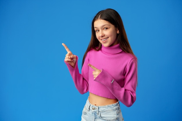 Teenager girl pointing to copy space with a finger over blue background