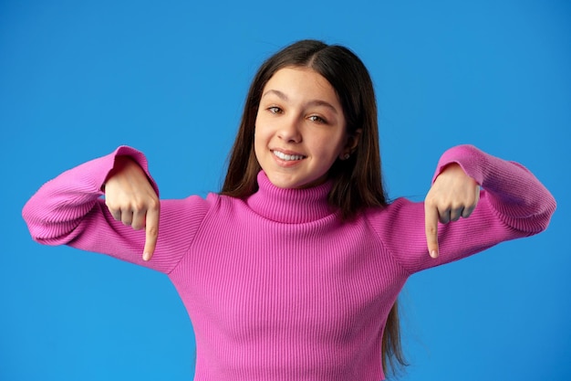 Foto ragazza adolescente che punta allo spazio della copia con un dito su sfondo blu