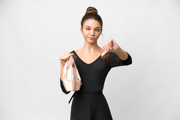 Teenager girl practicing ballet over isolated white background showing thumb down with negative expression