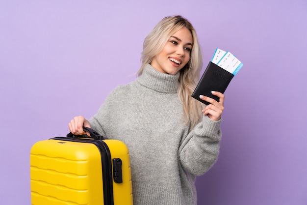 Teenager girl over purple wall in vacation with suitcase and passport