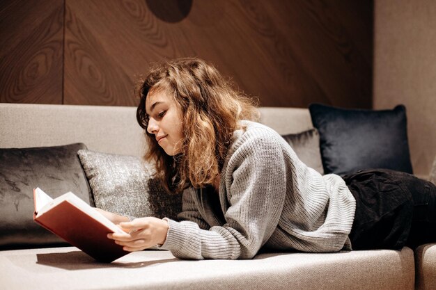Девочка-подросток читает книгу на диване дома