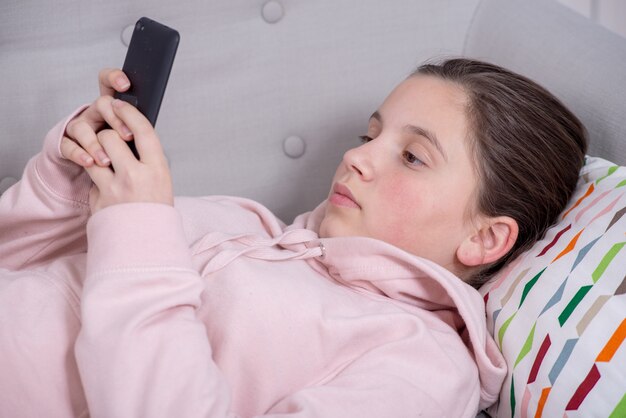 Teenager girl relaxes in the sofa and using phone