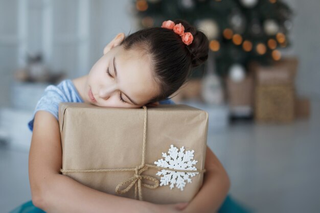 写真 10代の少女は、ギフトボックスを手にクリスマスツリーの近くに座っています。新年。嬉しい驚き。